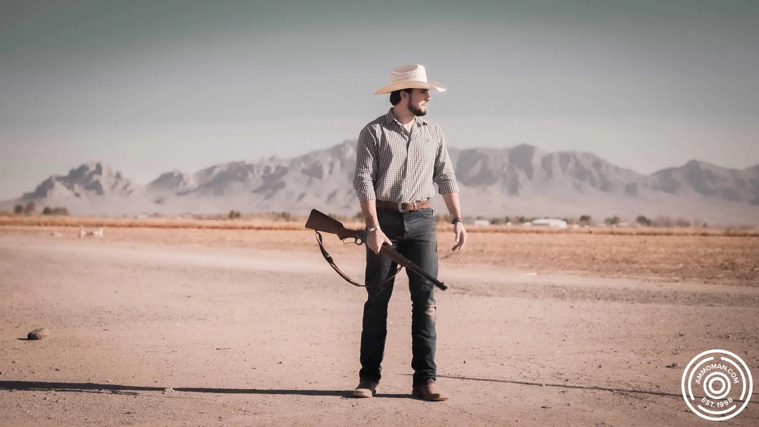 Man standing in desert with a 30-30 lever action rifle.