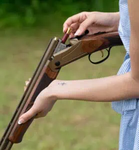 A female shooter loads 410 ammo into a break-action shotgun.